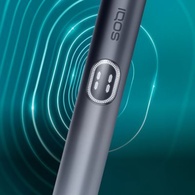 Das Bild zeigt eine Nahaufnahme des IQOS ILUMA i PRIME Holders in der Farbe Midnight Black. Das zylindrische Gerät trägt den Schriftzug ‚IQOS‘ und verfügt über einen Knopf mit halbkreisförmiger LED-Anzeige. Der Hintergrund besteht aus konzentrischen, geschwungenen Linien in Türkis- und Blautönen, die Tiefe und Bewegung erzeugen.