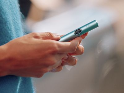 Ein IQOS ILUMA i Gerät in der Farbe Breeze Blue in den Händen einer Frau.