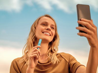 Žena kouká do mobilu a v ruce drží zařízení IQOS ILUMA i