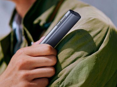 Eine Hand hält ein IQOS ILUMA i ONE in Midnight Black vor dem Oberkörper. 