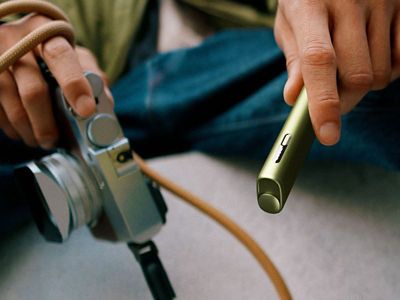 Nahaufnahme eines IQOS ILUMA i ONE Geräts in der Farbe Green und einer Kamera. 