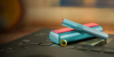 Blue IQOS ILUMA i PRIME cihazı, şarj cihazının üstündə, bükülü örtük və üzük ilə fərdiləşdirilmiş