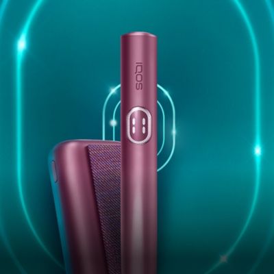 جهاز IQOS ILUMA i PRIME باللون النبيتي وشاحنه، على خلفية تركواز داكنة