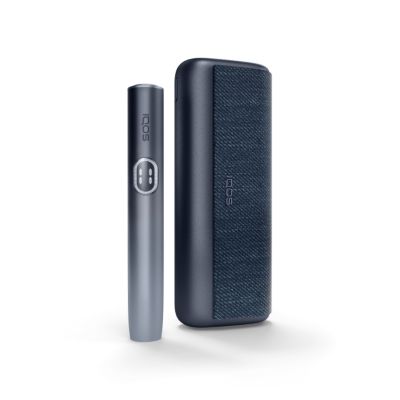 Das Bild zeigt den IQOS ILUMA i PRIME Holder und das IQOS ILUMA i PRIME Charger in einer schwarzen Farbvariante. Der Holder ist zylindrisch mit einem Knopf und zwei kleinen LED-Anzeigen sowie vertikalem ‚IQOS‘-Schriftzug. Das Charger ist rechteckig mit strukturierter Oberfläche und dient als Aufbewahrungs- und Ladeeinheit.
