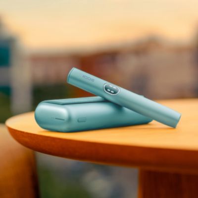 Držalo IQOS ILUMA i PRIME naprave v svetlomodri barvi Breeze Blue na žepnem polnilniku na mizi