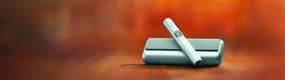 Green IQOS ILUMA i PRIME device above its charger, with red background