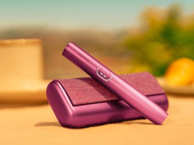 Устройство IQOS ILUMA i PRIME гранатово-красного цвета над зарядным устройством