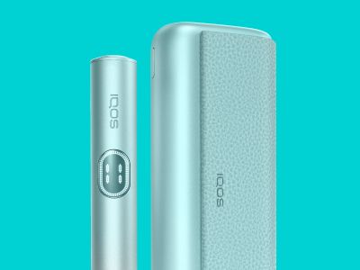 Устройство IQOS ILUMA i PRIME цвета Голубой бриз стоит рядом с зарядным устройством