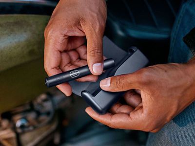 Eine Person nimmt den Holder eines IQOS ILUMA i in der Farbe Midnight Black aus dem passenden Pocket Charger.