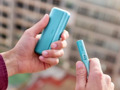 Ruka držící modré zařízení IQOS ILUMA i PRIME a nabíječku