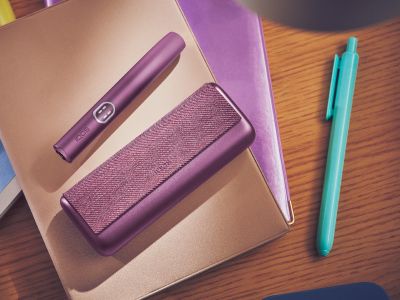 granátově rudé zařízení IQOS ILUMA i PRIME s nabíječkou na hnědém zápisníku