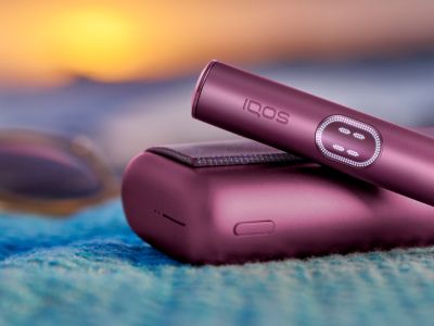 Granátově rudé zařízení IQOS ILUMA i PRIME s nabíječkou na modré látce