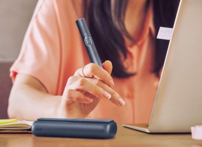 Fraut sitzt vor Laptop und hält IQOS ILUMA i PRIME Midnight Black in der Hand