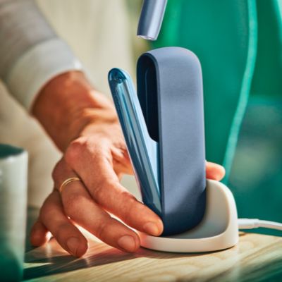 Une personne plaçant un chargeur de poche IQOS ILUMA dans une station de charge.