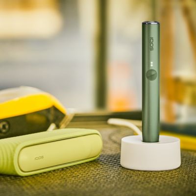 An IQOS ILUMA device in a charging station with a Pocket Charger on a table.