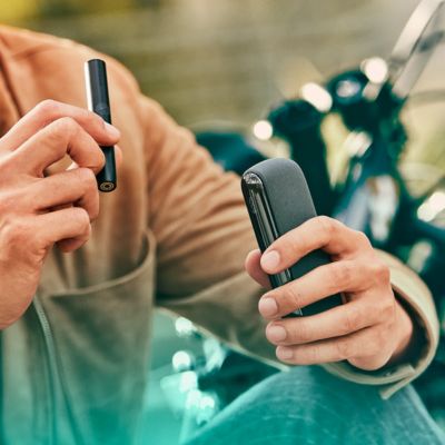 A person holding an IQOS ILUMA Pocket Charger and Holder. 