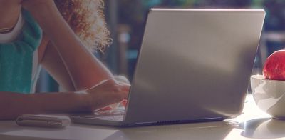 A close-up of someone working on their Mac resting on their arm while their IQOS ILUMA device lays next to them on the table