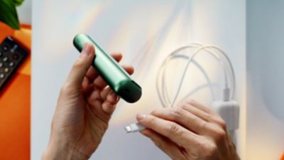 Unas manos conectan un Adaptador de Corriente a un IQOS ILUMA ONE.