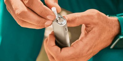 Hands inserting a TEREA stick into an IQOS ILUMA ONE device.