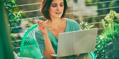 Una mujer sostiene un dispositivo IQOS ILUMA mientras mira hacia una computadora portátil.