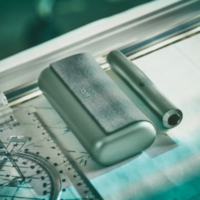 A Jade Green IQOS ILUMA PRIME Holder and Pocket Charger in a person's hands.