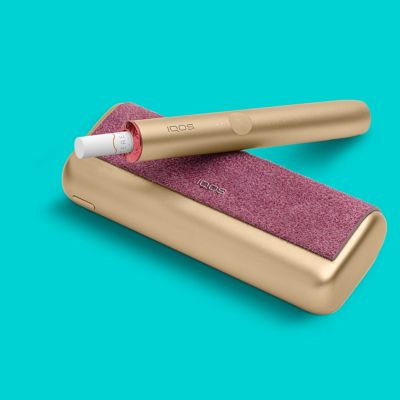 A gold and violet IQOS ILUMA device and its charger on a turquoise background