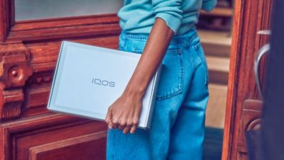 A person in jeans carrying a package from IQOS.