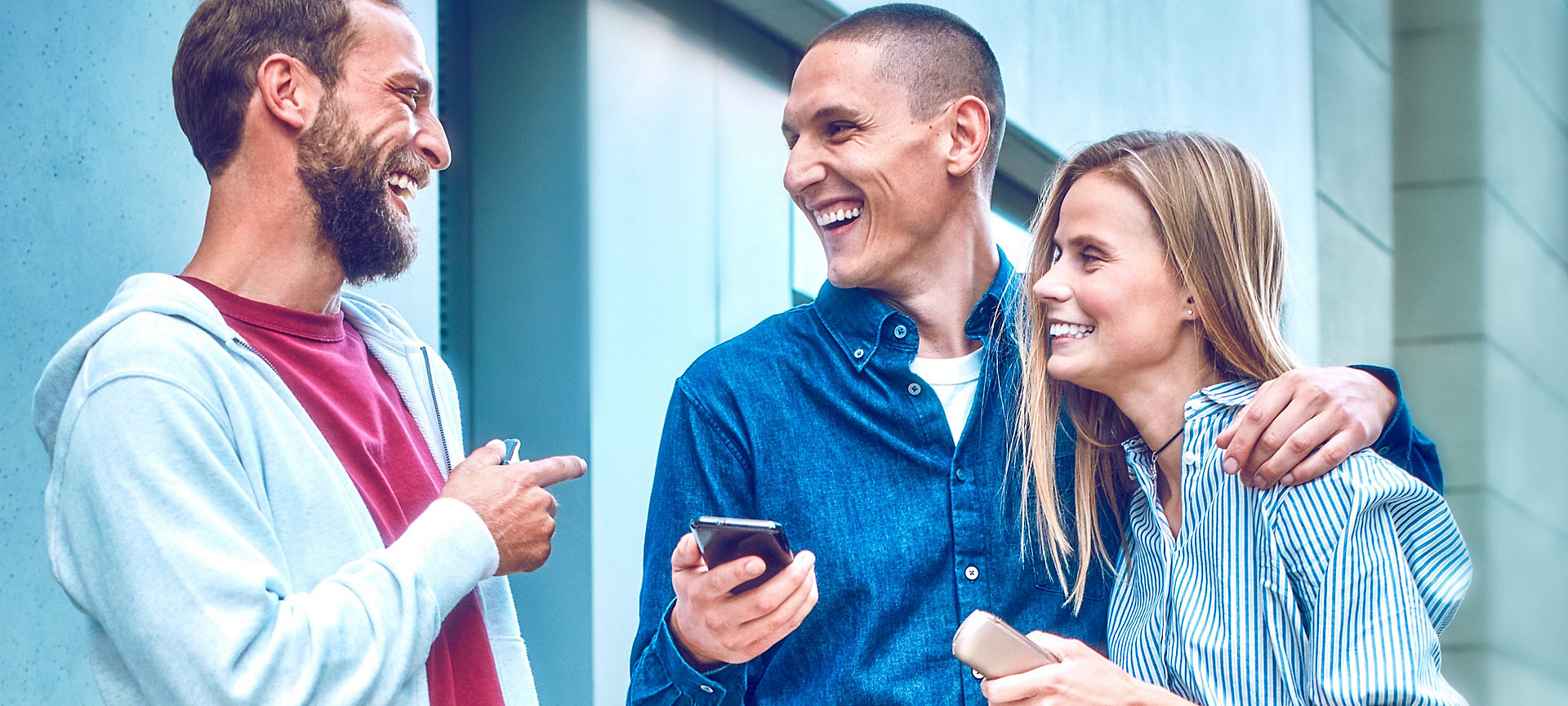 Dos personas que sostienen dispositivos IQOS ILUMA sonríen mientras su amiga mira la aplicación de IQOS en su teléfono móvil.