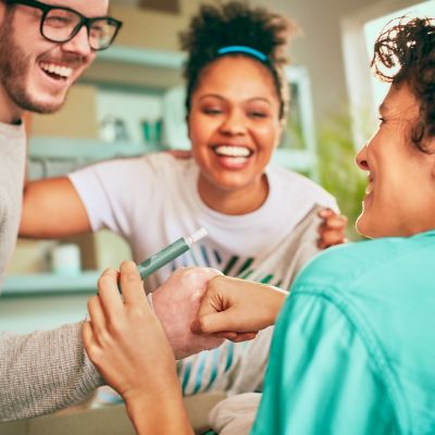 A man holding an IQOS device fist bumps his friend; a smiling woman looks on. 