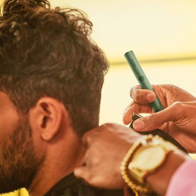 Un hombre a punto de cortarse el pelo con un barbero que sostiene un dispositivo IQOS ILUMA.