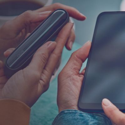Dos personas con teléfonos se sientan en una mesa; una de ellas sostiene también un Dispositivo IQOS ILUMA PRIME Azul