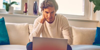A man sitting on a couch looking at a laptop.