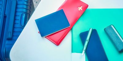 A woman sitting at a table next to her suitcase with a smartphone, passport and plane ticket.