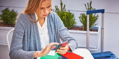 Mujer sentada en una mesa, con su celular, pasaporte y tiquete de avion