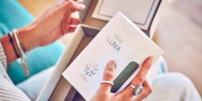 EIne Frau öffnet ein IQOS Paket und hält eine IQOS ILUMA Box in der Hand.