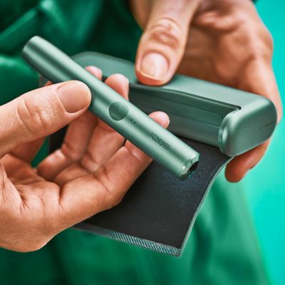 Two people fist bumping; one holds and IQOS ILUMA device.