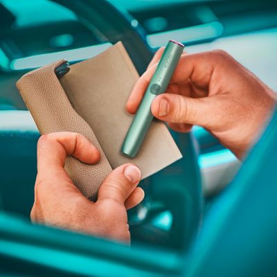 Seseorang meletakkan Pemegang IQOS ILUMA PRIME jade green ke dalam Pengecas Poket yang ditutup dengan balutan penuh