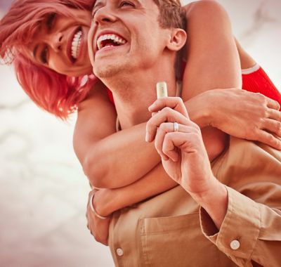 Un hombre que sostiene un dispositivo IQOS es abrazado por una amiga.