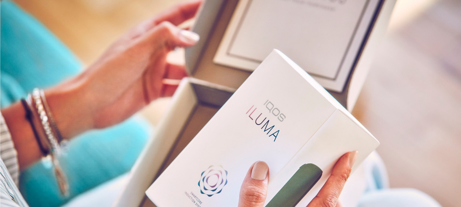 A person holding a box that contains a booklet on IQOS ILUMA.