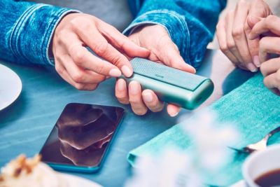 A person holding a Jade Green IQOS ILUMA PRIME Pocket Charger.
