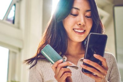 Žena drží Jade Green IQOS ILUMA kapesní nabíječku a sleduje svůj telefon.