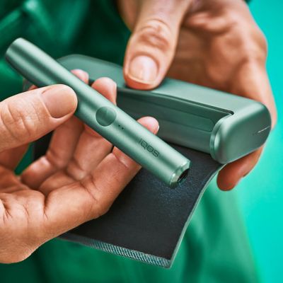 Close up of hands holding IQOS ILUMA jade green device.