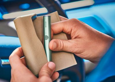 Gros plan d'une main prenant l'appareil IQOS ILUMA vert jade du support.