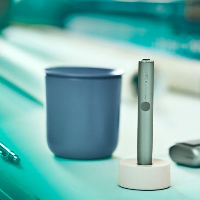 Jade green IQOS ILUMA device and charger on a desk.