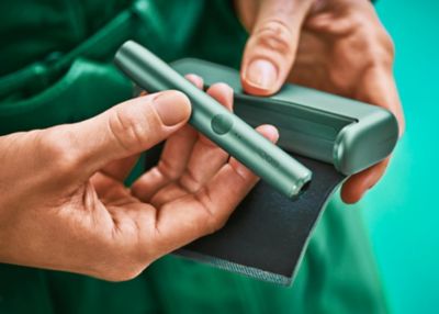 Gros plan des mains tenant un appareil vert jade IQOS ILUMA.