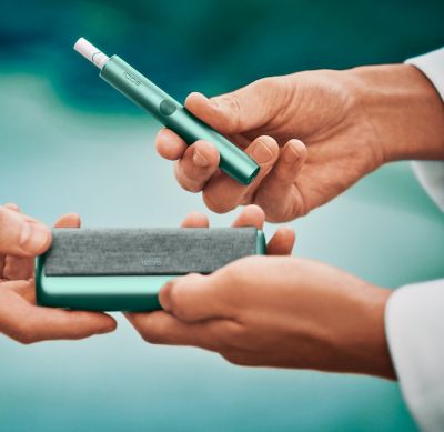 Close up of hands sharing an IQOS ILUMA device. 