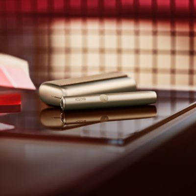 IQOS ILUMA PRIME dorado sobre mesa con vidrio