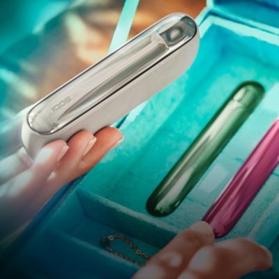 IQOS ILUMA en mano con carcasas laterales de fondo