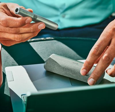 A man's hands opening a mid azure blue IQOS ILUMA device.