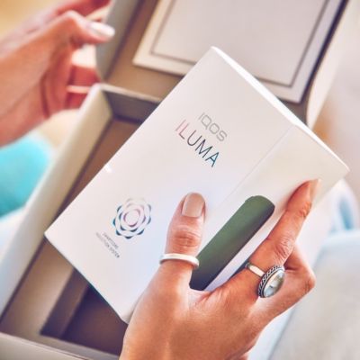 Manos de mujer con Kit de IQOS ILUMA abriéndolo.